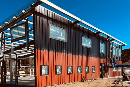 Commercial steel building construction showing exposed steel framework and two-tone corrugated metal siding with windows installed in Colorado